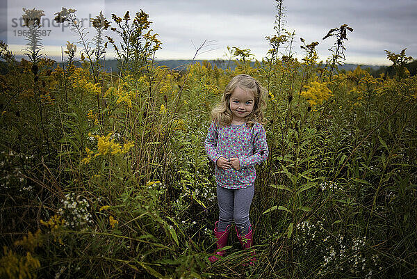 Kleines Mädchen lächelt im Feld der Wildblumen mit rosa Stiefeln