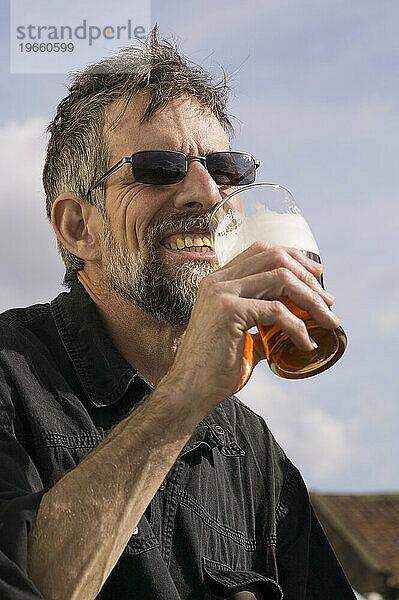 Ein Mann mit Bart trinkt ein Pint Bier in der Stadt Helmsley in England.