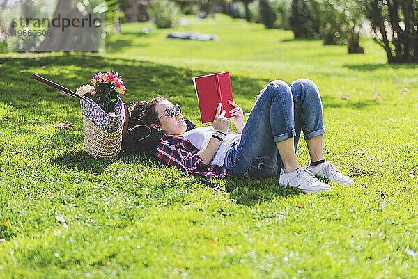 Seitenansicht einer glücklichen Hipster-Frau  die an einem sonnigen Tag im Gras liegt