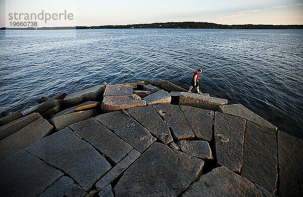 Ein Mann geht am Rande eines Felsvorsprungs mit Blick auf ein großes Gewässer.