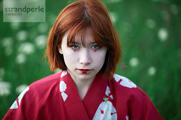 Porträt eines Mädchens mit roten Haaren im Kimono und weißem Make-up im Freien