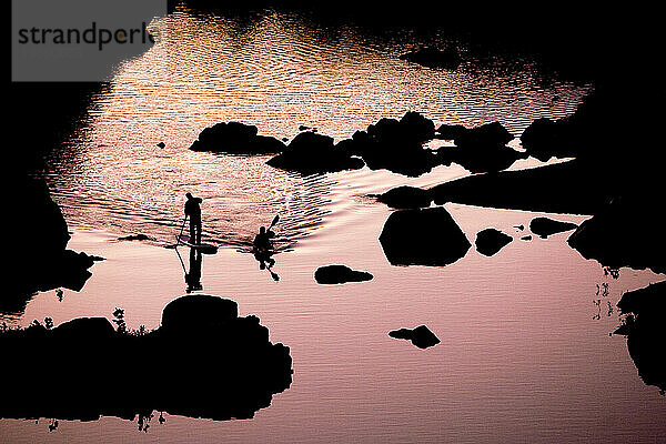 Silhouette eines Kajakfahrers und eines Stand-Up-Paddleboarders auf ruhigem Wasser bei Sonnenuntergang.