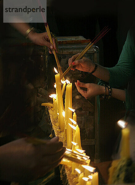 Brennende Kerzen und Hände  die Weihrauch an die Flamme halten