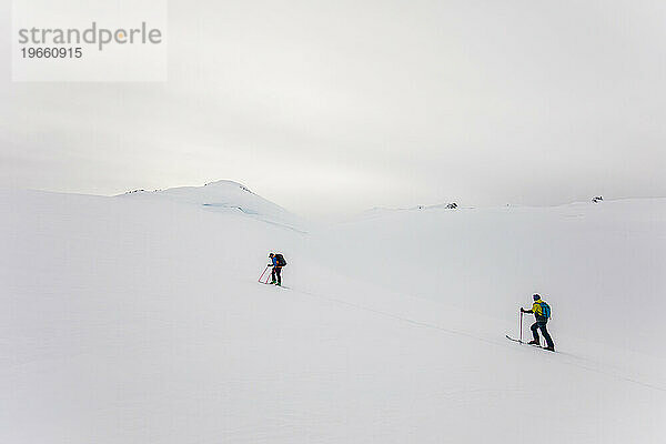 Seitenansicht von zwei Skifahrern  die sich dem Berggipfel nähern