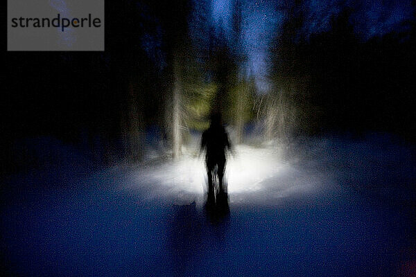 Die Silhouette eines Mannes liegt im Schnee und läuft durch Bäume auf dem Mt. Rose  Nevada. (Bewegungsunschärfe) (Weichzeichnung)