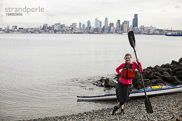 Ein junges Mädchen steht an einem bewölkten Tag im Puget Sound vor der Küste der Innenstadt von Seattle neben ihrem Kajak.