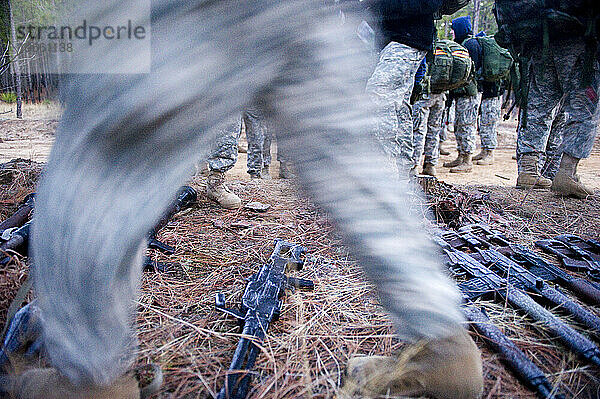 Soldaten laufen im frühen Morgenlicht umher und sammeln Waffenattrappen für eine Feldübung.