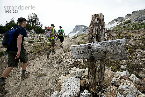 Drei Jungen gehen am Schild zum Eagle Cap Summit vorbei  mit dem Gipfel im Hintergrund in der Eagle Cap Wilderness im Nordosten Oregons.