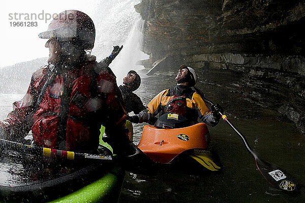 Kajakfahrer hängen in einem Zwei-Personen-Kajak unter einem Wasserfall herum.