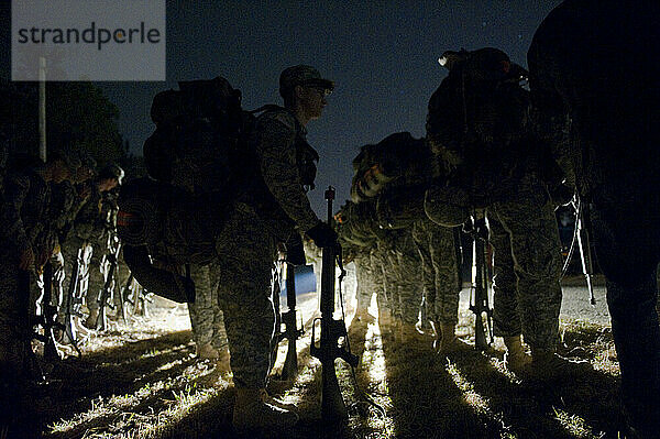 Während einer Feldübung stehen Soldaten mitten in der Nacht in Formation in der Nähe einer unbefestigten Straße.