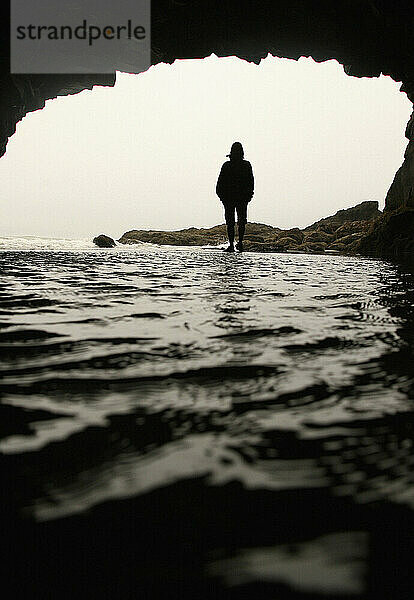 Eine Frau steht im Wasser als Silhouette am Eingang einer Höhle in Oregon.