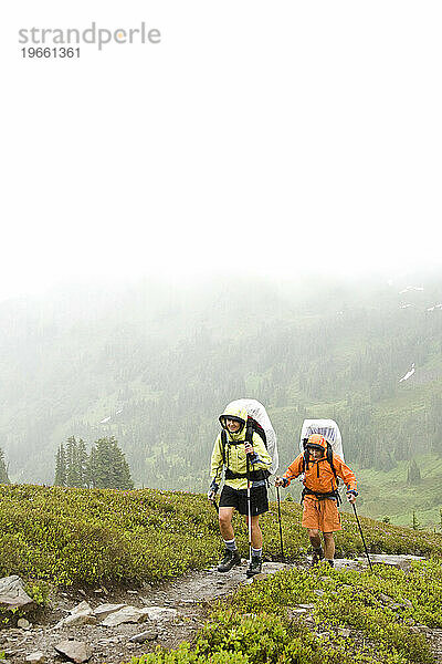 Zwei Personen wandern im Regen mit Mänteln und Rucksackhüllen