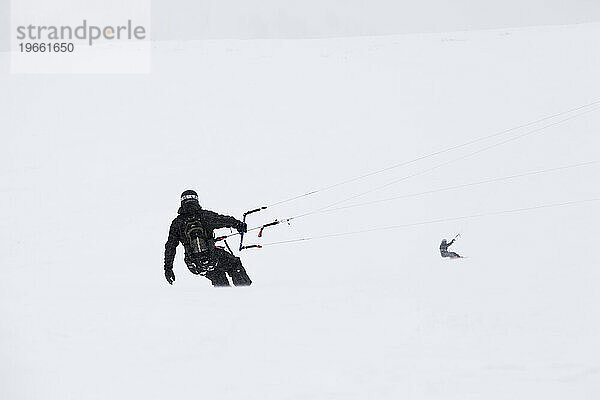 Silhouetten zweier Snowkiter  die in einem Whiteout fahren.