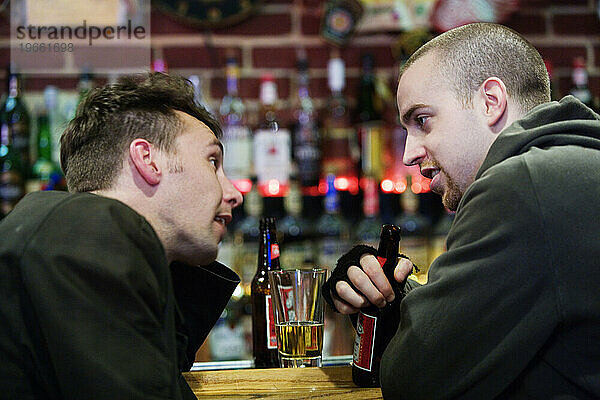 Zwei Männer sitzen an einer Bar und unterhalten sich.