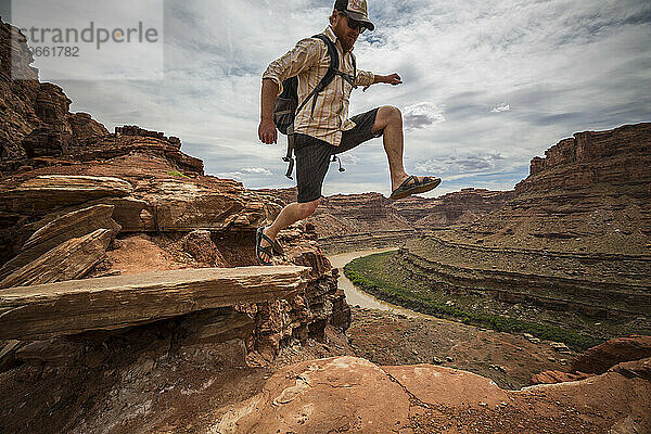 Ein Mann springt von einem Felsen über einem Fluss in der Wüste.