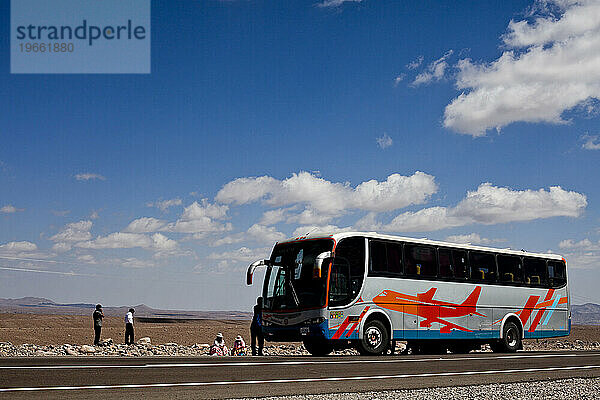 Ein Personenbus holt zwei Personen am Straßenrand in der Atacama-Wüste in Bolivien ab.
