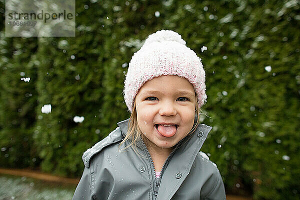 Süßes junges Mädchen fängt draußen Schneeflocken mit der Zunge.