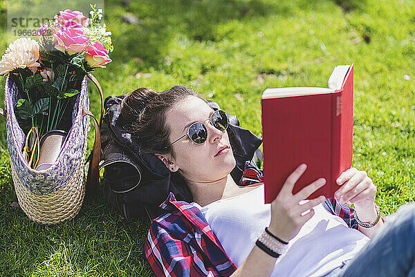 Seitenansicht einer glücklichen Hipster-Frau  die an einem sonnigen Tag im Gras liegt