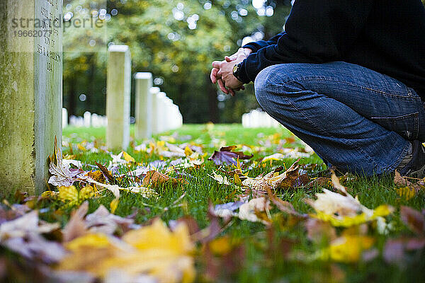 Ein junger Mann kniet nieder  während er einen der vielen mit Herbstblättern geschmückten Grabsteine ??auf dem Fort Lawton Cemetery in Seattle  WA  liest.