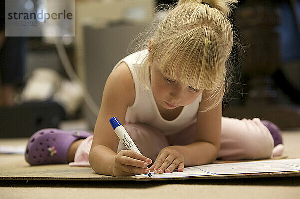 Ein Vorschulmädchen konzentriert sich auf ihre Kunstwerke und zeichnet mit einem Filzstift.