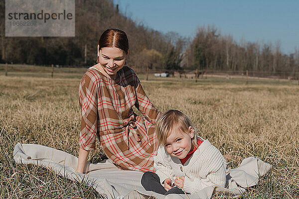 Rothaarige Frau mit Kind sitzt auf einem Plaid auf einem trockenen Feld
