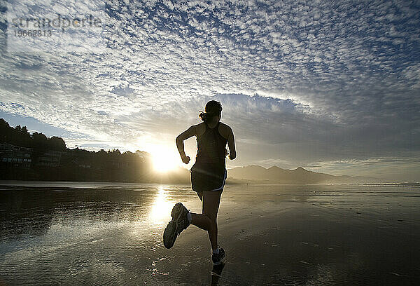 Eine Frau läuft bei Sonnenaufgang am Strand.