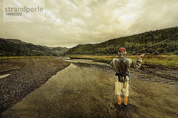 Ein Mann beim Fliegenfischen an einem Fluss in den Bergen. Grunge-Ebeneneffekt angewendet.