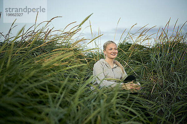 Zufriedene blonde Frau sitzt auf dem ländlichen Gebiet