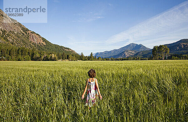 Ein junges Mädchen  die Tochter eines Bauern  geht an einem sonnigen Morgen mit dem Rücken zur Kamera durch ein Feld.