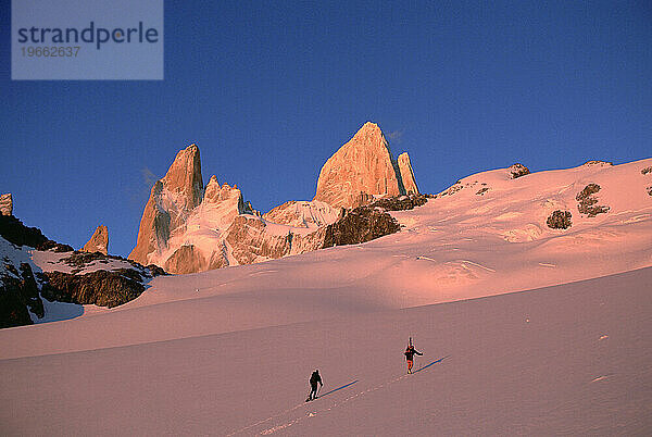 Männer überqueren einen Gletscher in Richtung roter Gipfel.