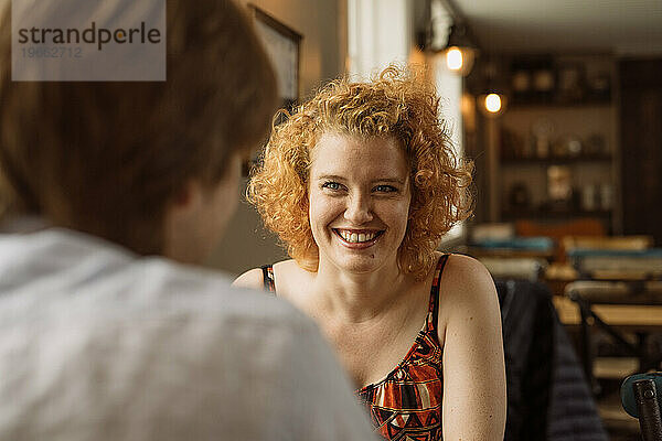 Fröhliche junge Frau mit einer Freundin  die am Tisch im Café sitzt