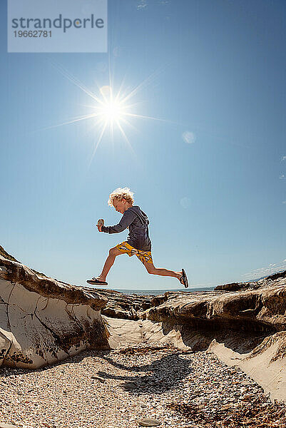 Aktives Kind springt an sonnigem Tag an der felsigen Küste