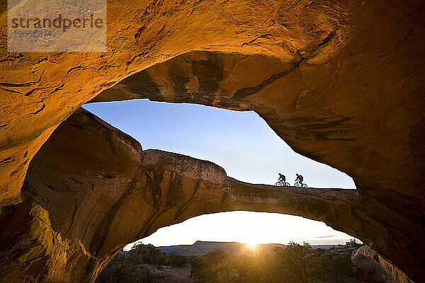 Ein Mann und eine Frau reiten über einen natürlichen Felsbogen in der Wüste in der Nähe von Moab  Utah.