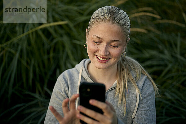 Fröhliche Frau benutzt Smartphone gegen grüne Pflanzen