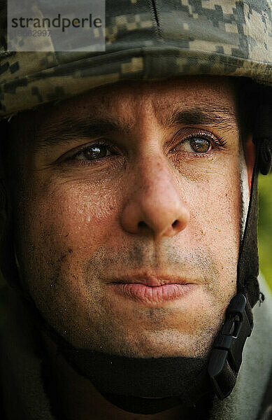 Ein Soldat der U.S. Army Guard demonstriert das richtige Tragen von Körperschutz. Der Soldat verzieht leicht das Gesicht  während sich Schweiß auf seinen Augenlidern sammelt.
