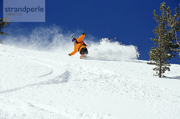Ein Mann beim Snowboarden an einem Bluebird-Powder-Tag in einem Bergresort in der Nähe von South Lake Tahoe  Kalifornien.