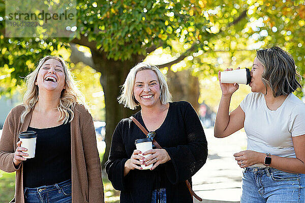 Drei Frauen mit Kaffeetassen gehen lachend