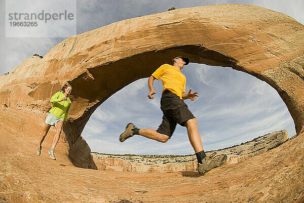 Zwei Menschen laufen unter Wilson Arch  Moab  Utah.