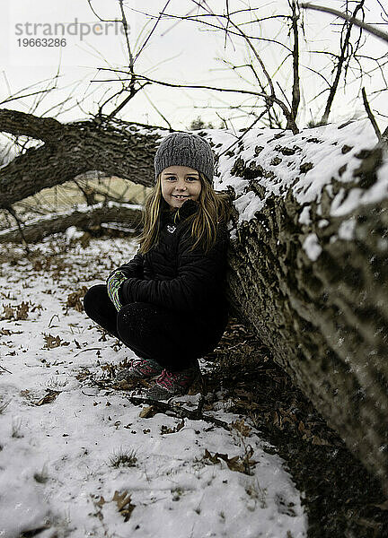 Fröhliches junges Mädchen lächelt im verschneiten Wald im Winter