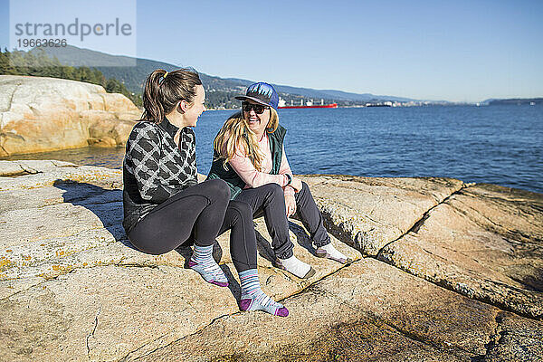 Freundinnen sitzen am Strand von Vancouver und unterhalten sich.