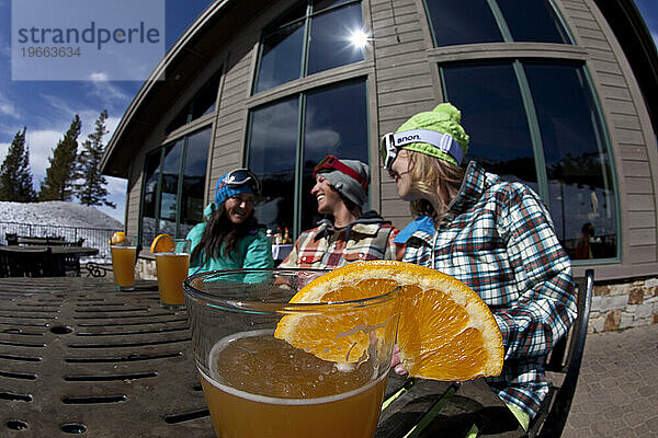 Drei Freunde trinken ein Bier auf der Außenterrasse eines Skigebiets.