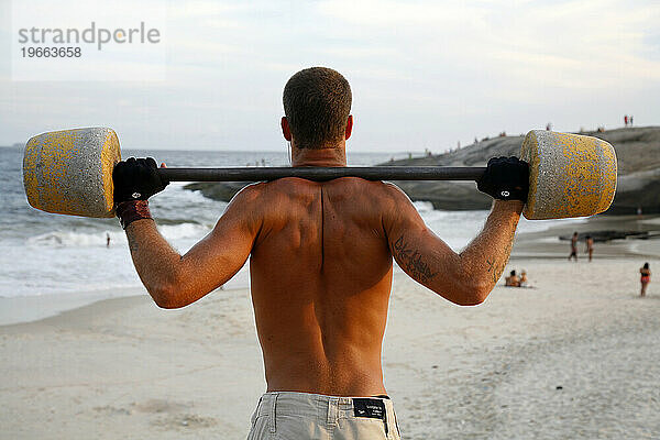 Mann trainiert in einem öffentlichen Fitnessstudio im Freien am Strand von Arpoador  Rio de Janeiro  Brasilien.