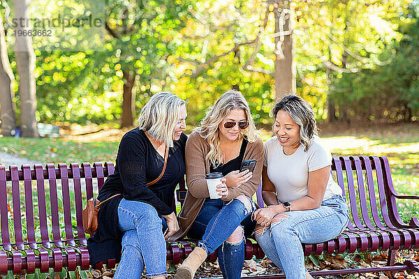 Drei Frauen sitzen auf einer Bank und schauen auf das Telefon einer Freundin
