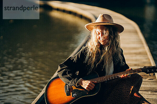 Frau mit Gitarre am See im Herbst