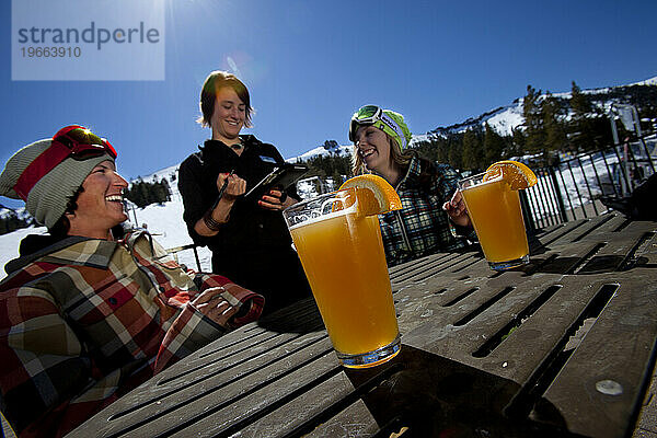 Junges Paar bestellt Essen und Bier auf der Außenterrasse eines Skigebiets.