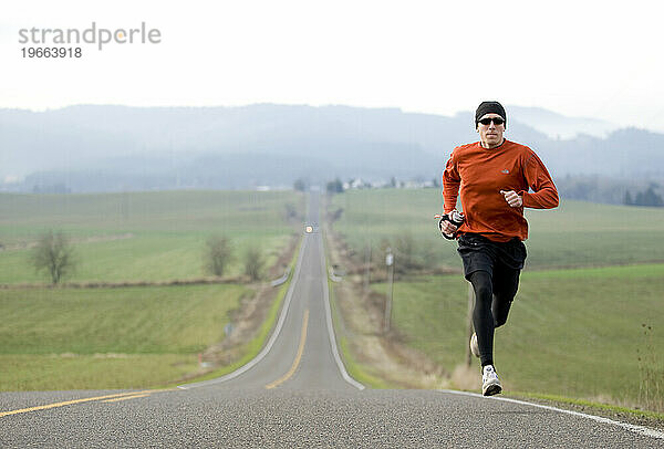 Ein Mann joggt eine Landstraße entlang mit einem wunderschönen sanften Hügel im Hintergrund.
