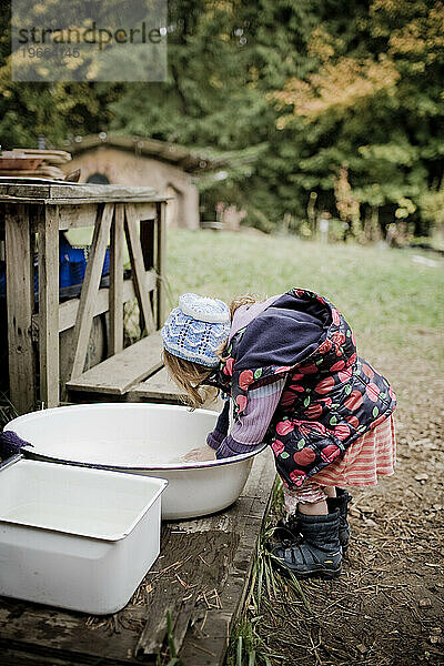 Ein rothaariges Mädchen  das sich für das kalte Wetter warm eingepackt hat  wäscht sich in einem Waschbecken die Hände.