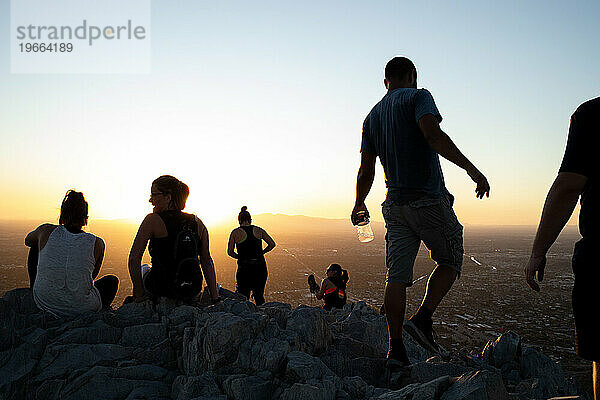 Silhouetten von Menschen drängen sich bei Sonnenuntergang auf dem Berggipfel