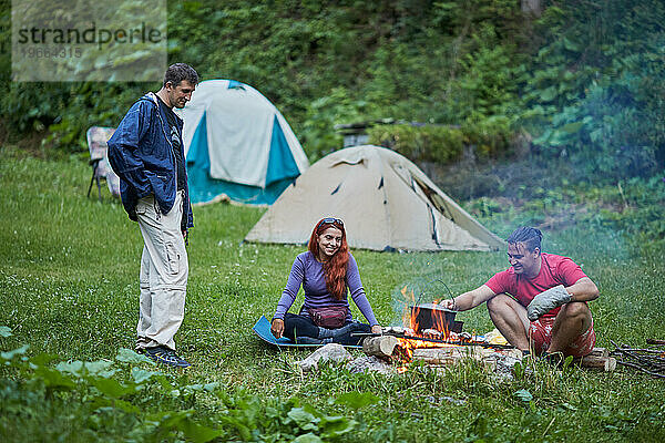 Freunde in der Nähe von Lagerfeuer in der Campingzone