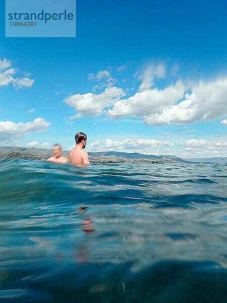 Zwei Jungen schwimmen im See mit blauem Himmel